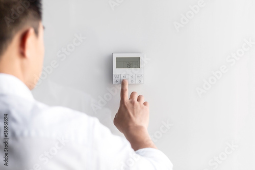 Close-up photo. The hand of a young man in a white shirt turns on the control buttons of the air conditioner hanging on the wall. Standing on the left