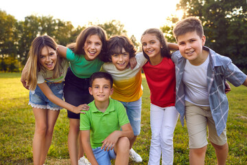 Kids having fun outdoors in summer. Group portrait of happy little school children in the park. Bunch of cheerful friends posing for a group photo, hugging, looking at the camera and smiling