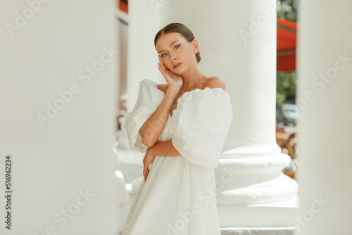 A young beautiful woman in a white dress near the columns