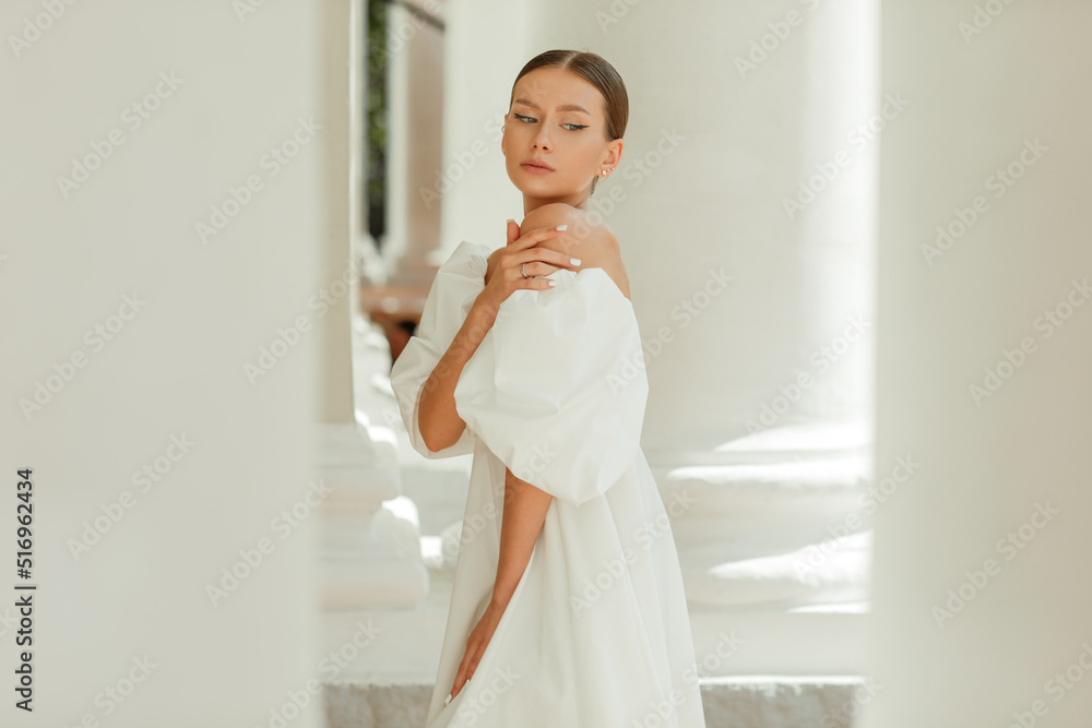 A young beautiful woman in a white dress near the columns