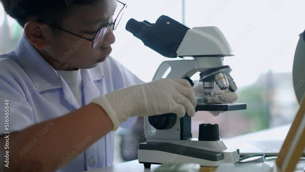 Asian scientist boy looking through microscope and lab equipment Asian scientist boy looking through microscope and lab equipment