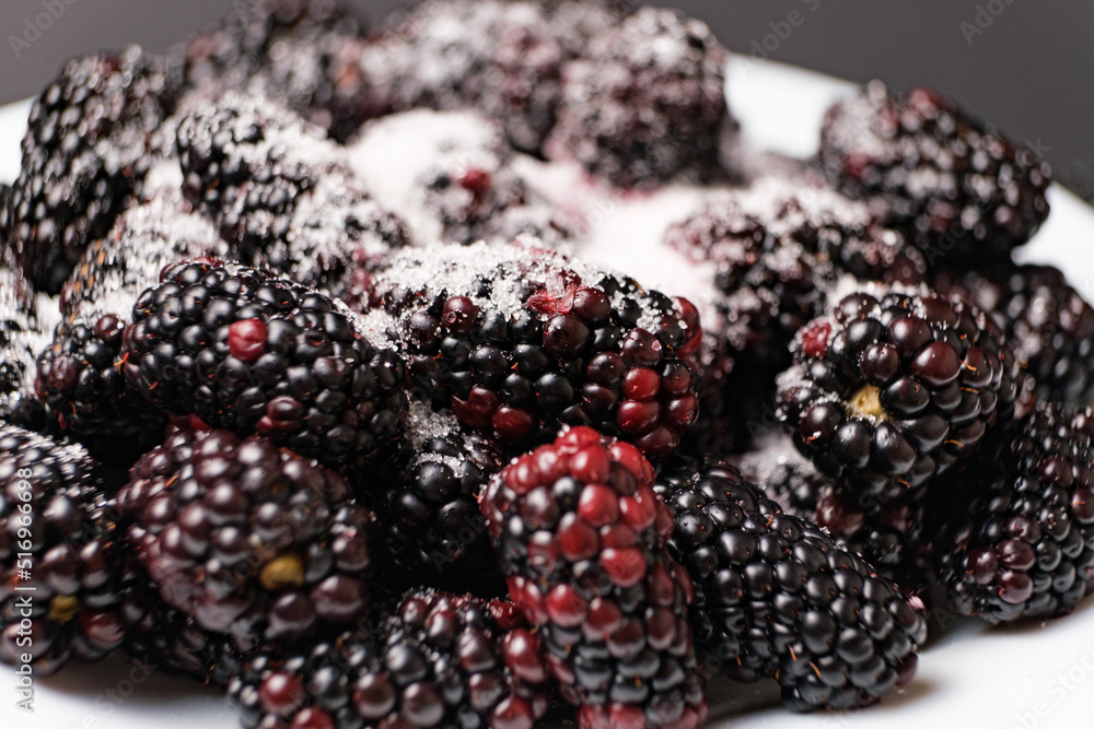 Blackberries sprinkled with sugar in a plate on a black background, close-up view from the side. Blackberries sprinkled with sugar in a plate on a black background, close-up view from the side.