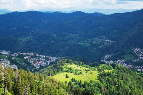 Mountain valley sheltered by vegetation and spruce forests with village of Smolyan with meadows where sheep graze