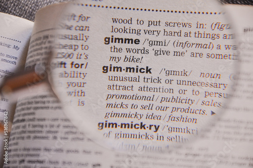 The definition of the word Gimmick in a dictionary, under magnifying glass, translator and language concept photo