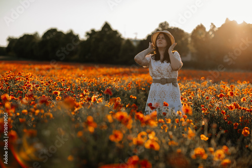 Fototapeta Naklejka Na Ścianę i Meble -  Scenic picturesque of beautiful girl in white and beige dress and straw hat in poppy field at sunset, Portrait of romantic young woman with flowers, body positivity, Selective focus natural light