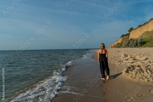 Woman wearing black dress walking on beach. See view