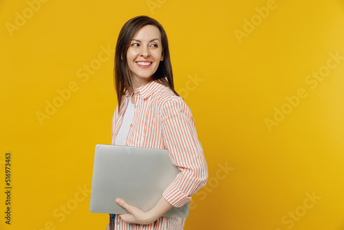 Side view young happy smiling secretary copywriter woman she 30s in striped shirt white t-shirt hold use work on laptop pc computer look aside on workspace area isolated on plain yellow background