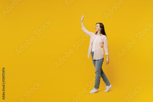 Full body side view young happy smiling woman she 30s wear striped shirt white t-shirt walking going strolling waving hand isolated on plain yellow background studio portrait People lifestyle concept © ViDi Studio
