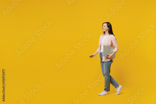 Fotobehang Full body side view young happy smiling woman she 30s wears striped shirt white t-shirt hold use closed laptop pc computer walk go isolated on plain yellow background studio
