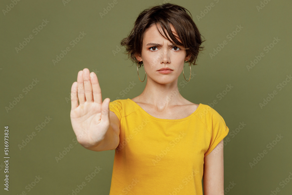 Young sad strict serious woman she 20s wearing yellow t-shirt showing stop gesture with palm refusing reject isolated on plain olive green khaki background studio portrait. People lifestyle concept. Young sad strict serious woman she 20s wearing yellow t-shirt showing stop gesture with palm refusing reject isolated on plain olive green khaki background studio portrait. People lifestyle concept.