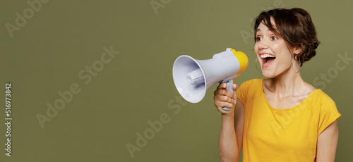Young expressive woman she 20s wear yellow t-shirt hold scream in megaphone announces discounts sale Hurry up isolated on plain olive green khaki background studio portrait People lifestyle concept.