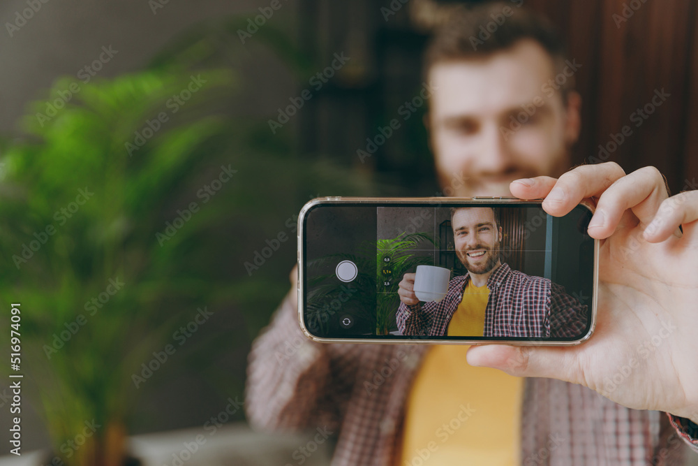 Young man 20s he wear shirt doing selfie shot on cell phone with cup sit alone at table in coffee shop cafe relax rest in restaurant during free time indoors. Freelance mobile office business concept.