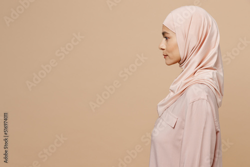 Side view young arabian asian muslim woman 30s she wearing abaya hijab pink clothes isolated on plain pastel light beige background studio portrait. People uae middle eastern islam religious concept.