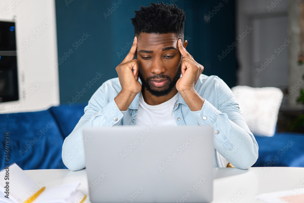 Tired male office employee holding hands at his head while looking at the laptop screen, feeling boring and angry. Bored multiracial man in smart casual shirt sitting at the desk Tired male office employee holding hands at his head while looking at the laptop screen, feeling boring and angry. Bored multiracial man in smart casual shirt sitting at the desk