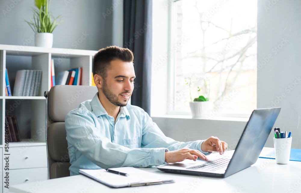 Young Man Works while Sitting in front of a Computer at Home. The Workplace of a Professional Worker, Freelancer or Student. Distance Work and Education Concept. Young Man Works while Sitting in front of a Computer at Home. The Workplace of a Professional Worker, Freelancer or Student. Distance Work and Education Concept.