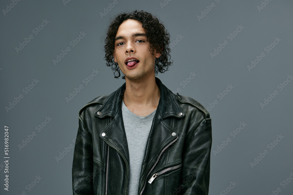 Obraz premium Cute attractive stylish tanned curly man leather jacket posing isolated on over gray studio background. Cool fashion offer. Huge Seasonal Sale New Collection concept. Copy space for ad