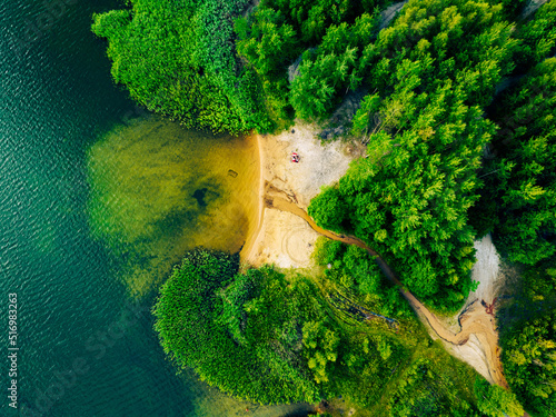 Fototapeta Naklejka Na Ścianę i Meble -  Summer holiday at the green lake. Rest on the beach, leisure time. Aerial view of small hidden beach surrounded by greenery.