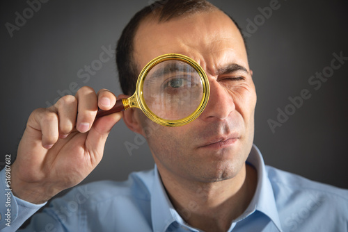 Caucasian man holding magnifying glass and looking at camera.