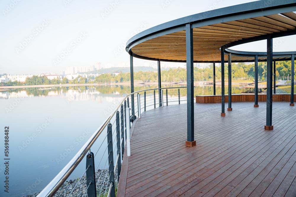 Wooden pier of round shape on the river bank, park for walking on the pond, country house with a view of the lake, art object in the city, a place for people to relax, relaxation and silence