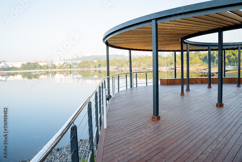 Wooden pier of round shape on the river bank, park for walking on the pond, country house with a view of the lake, art object in the city, a place for people to relax, relaxation and silence © Aleksey