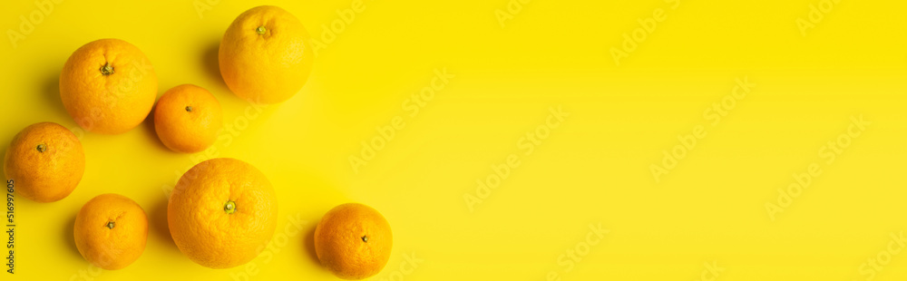 Top view of ripe mandarins and oranges on yellow background, banner.