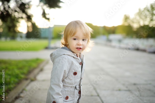 Funny toddler boy having fun outdoors on sunny autumn day. Child exploring nature. Kid walking in a city park.