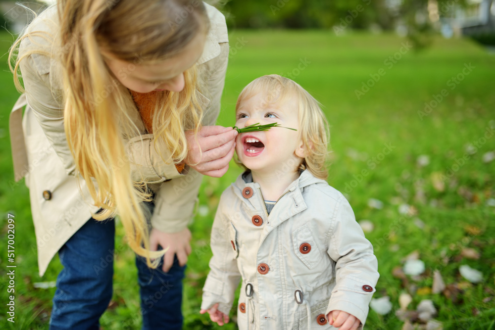 Funny toddler boy and his older sister having fun outdoors on sunny autumn day. Children exploring nature. Kids walking in a city park. Funny toddler boy and his older sister having fun outdoors on sunny autumn day. Children exploring nature. Kids walking in a city park.