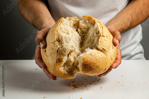 Mens hands break a loaf of round wheat bread made with sourdough, showing the inner texture