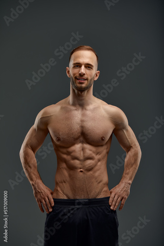 Young muscular caucasian man looking at camera and showing his naked torso while posing shirtless isolated over grey background. Sports, workout, bodybuilding concept