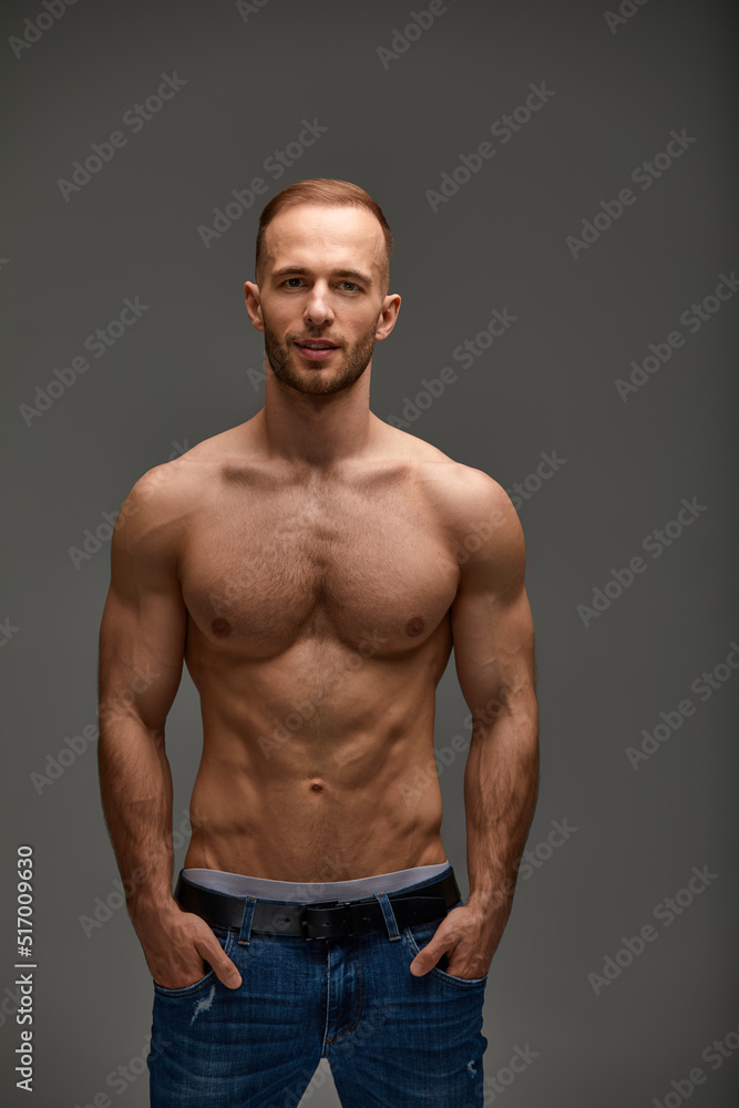 Portrait of a handsome young guy model a shirtless with a muscular healthy body, showing off his biceps muscles on a gray background