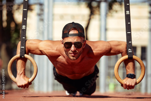 Muscular sportsman exercising on outdoor gymnastic rings in outdoor gym. Hands at rings dipping man doing exercise using rings