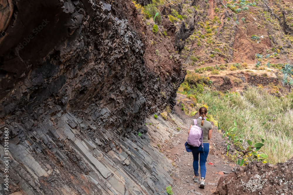 Woman walking along rock formation wall in the Canyon Barranco de Afur, Anaga park, Tenerife, Canary Islands, Spain, Europe. Panoramic hiking trail from Afur to Taganana in Anaga massif. Geology
