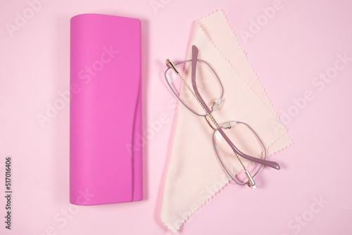 Pink frame womens glasses with glasses cleaning cloth and case on a pink background.