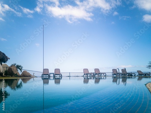 Fototapeta View of a swimming pool reflecting beach chairs and an alcove