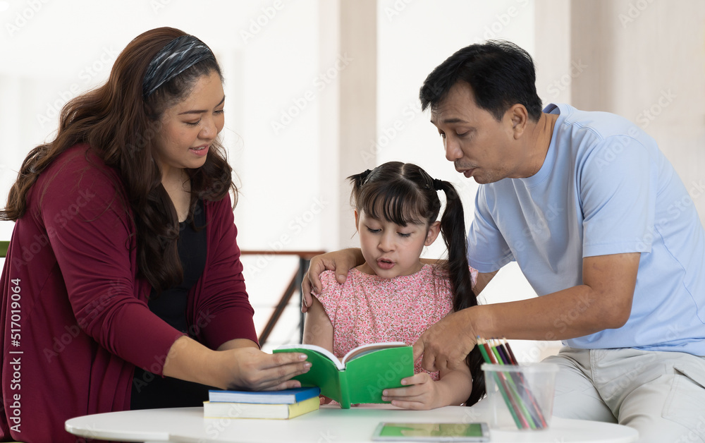 Diverse asian family with child daughter reading a book together at home. Smiling parents and teen daughter spending time together. Diverse asian family with child daughter reading a book together at home. Smiling parents and teen daughter spending time together.