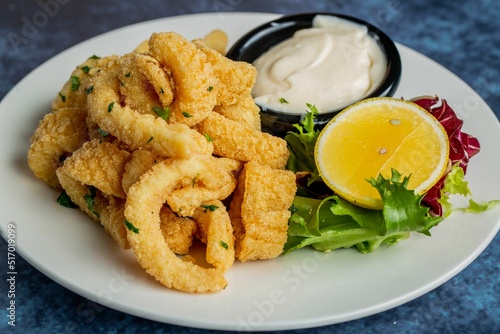 Closeup of a plate of Fried squid served with sauce and lemon slice on blue table photo