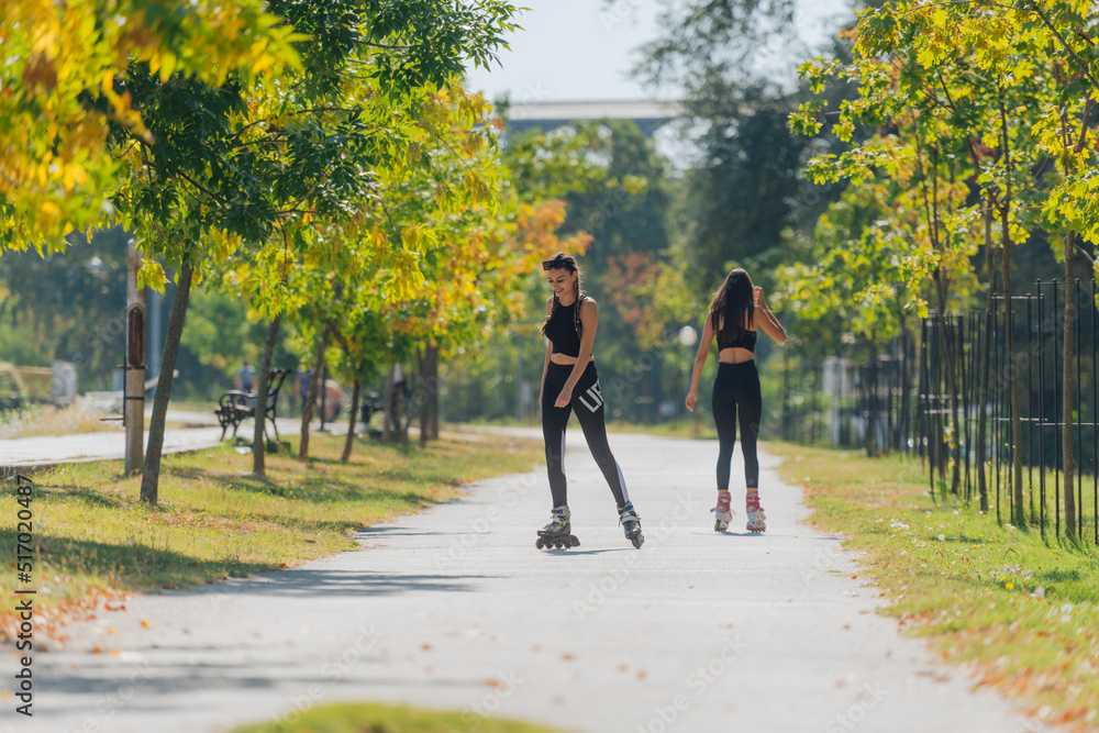 Obraz premium Full body portrait of happy sportswomen rollerskating in the park on a sunny day