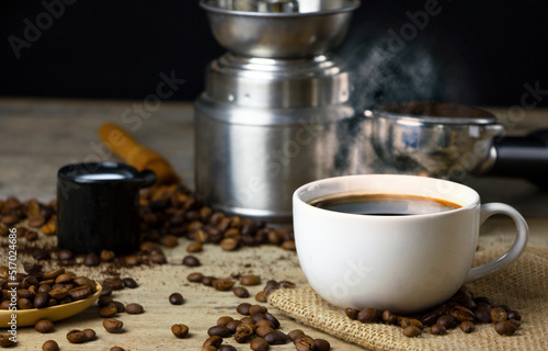 Cup of black Americano coffee on a wooden table with a pile of roasted Arabica coffee beans on black background.