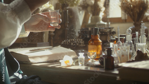 A close-up of a perfumer at his desk looking for a new fragrance. Vintage cinematic concept. Sunny day in the workshop. Lots of ingredients, glass flasks on the table. Concept of perfumery photo