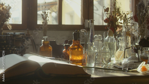 Close-up of a perfumer's workplace. Vintage cinematic concept. Sunny day in the working workshop. Lots of ingredients, a book, glass flasks on the table. Depth of field