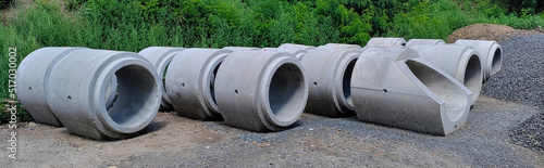 Wide photo of concrete sewage pipes in the park waiting to be put underground. They are sitting on the crushed stones.