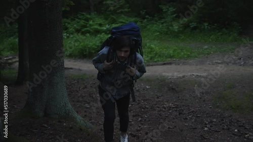 A tourist with a backpack walks through the night forest up the hill. His back is bent from the weight of the backpack. Slow motion 4k footage