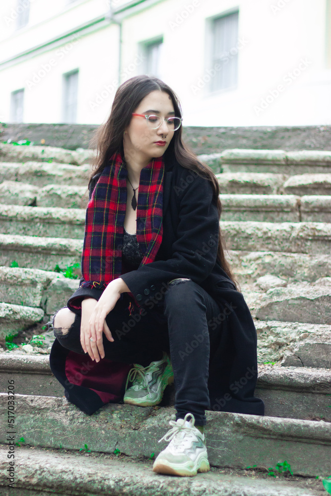 A young woman wearing a red hat, red scarf and a black coat is sitting on stairs going up at the street A young woman wearing a red hat, red scarf and a black coat is sitting on stairs going up at the street