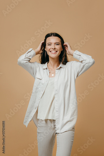 Cheerful happy young beautiful girl looking at camera, smiling, laughing over beige background.
