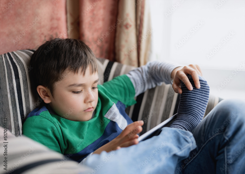 Portrait kid playing game on tablet sitting on sofa, Young boy reading or doing homework online on internet at home,Child watching cartoon online on digital pad.Home education,Back to school concept