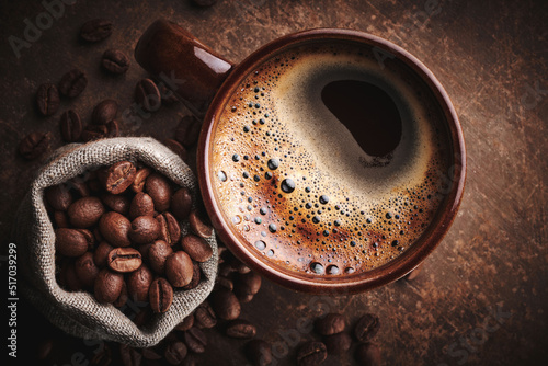 Composition of freshly brewed cup of coffee and roasted coffee beans in bag on brown background