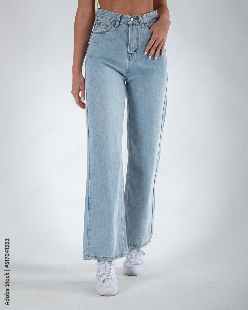 Sexy girl legs and feet in blue jeans pants and white sneakers in light gray background 