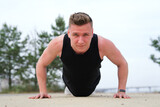 Portrait of handsome sportive fit fitness man, athlete, athletic guy doing push ups workout exercise on ground, training outdoors at summer sunny day in park. Healthy lifestyle. Open air gym