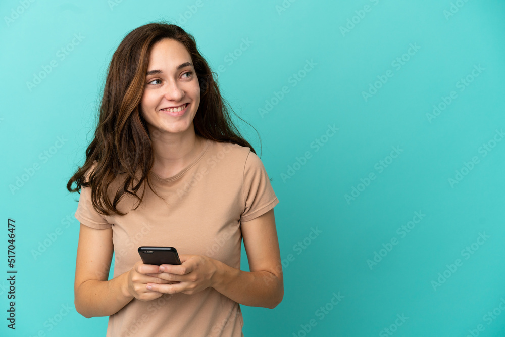 Young caucasian woman isolated on blue background using mobile phone and looking up Young caucasian woman isolated on blue background using mobile phone and looking up