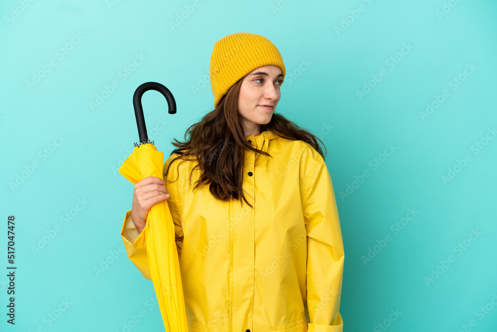 Young caucasian man holding an umbrella isolated on blue background looking side Young caucasian man holding an umbrella isolated on blue background looking side